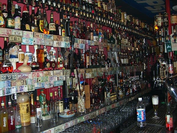 Die Regalwand hinter dem Tresen: Flaschen bis unter die Decke auf rotem Regal, an jeder Regalkante Geldscheine aus aller Welt.
